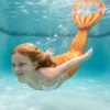 Queue de sirène Orange Attina Enfant portée par une fillette en mouvement sous l'eau, rayons de soleil